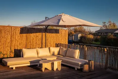 a couch sitting on a deck with an umbrella at Waterfront tiny home with spacious garden in Vinkeveen