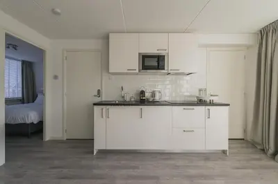 a kitchen with white cabinets and a bed in a room at Strand 122 Appartement in Egmond aan Zee