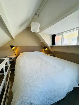 a bedroom with a large white bed with a window at Cosy summerhouse in Noordwijk aan Zee