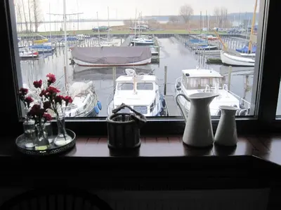 a window with a view of a marina with boats at Studio Vúr de Diek in Spakenburg