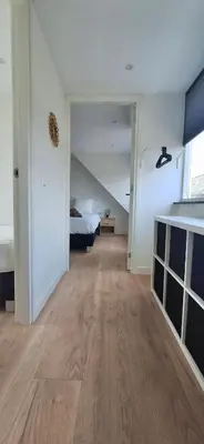 an empty room with a bed and a room with wood floors at Miles in Egmond aan Zee