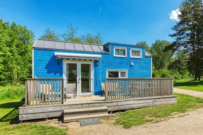 a blue tiny house with a wooden porch at Blue Tiny House with HotTub in Zeewolde