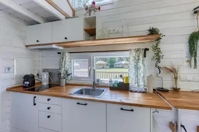 a kitchen with white cabinets and a sink and a window at Blue Tiny House with HotTub in Zeewolde