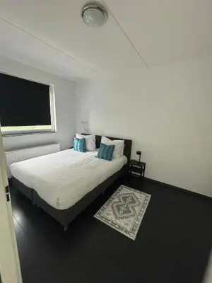 a bedroom with a bed with white sheets and blue pillows at In Almere, Close to Amsterdam in Almere