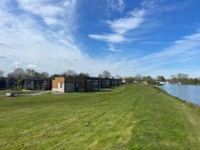 a grassy field next to a river with buildings at EuroParcs Kagerplassen in Warmond