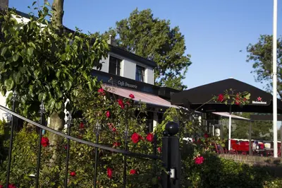 a building with red roses in front of a fence at Café Brasserie Het Heerenhuis in Het Kalf