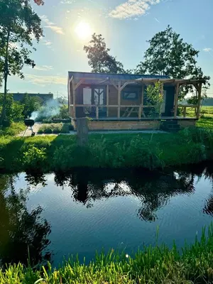 a house on the edge of a pond with the sun in the background at TinyHouse Ochtendgloren in Haastrecht