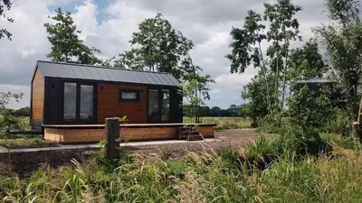 a tiny house with a black roof in a field at TinyHouse Ochtendgloren in Haastrecht