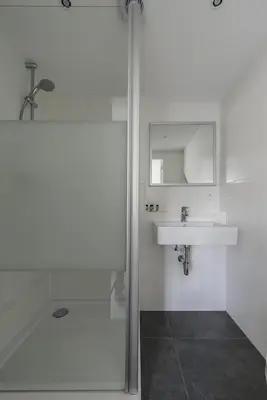 a white bathroom with a shower and a sink at Strandhuis 122 Studio in Egmond aan Zee