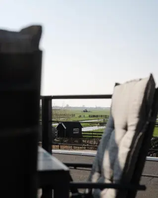 a chair sitting on a balcony with a view of a farm at B&B Hartenlust kamer de Hooizolder in Bodegraven