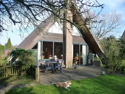 a woman sitting at a table with a dog in the yard at Bungalowpark West Friesland in Opmeer