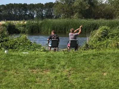two people sitting in chairs in front of a river at De Meerkoet in Nieuwe-Niedorp