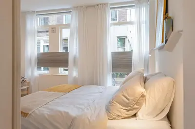 a white bed in a room with two windows at Studio Carlos in Haarlem
