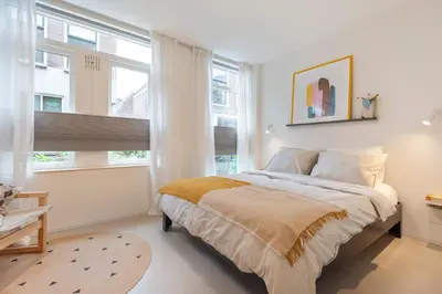 a white bedroom with a bed and two windows at Studio Carlos in Haarlem