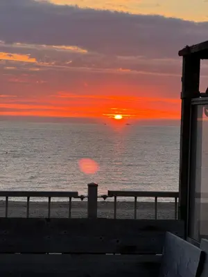 a sunset over the ocean with benches on the beach at Huisje Aangenaam in Dirkshorn