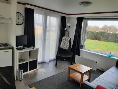 a living room with a large window and a chair at Chalet dichtbij zee en duinen in Heemskerk