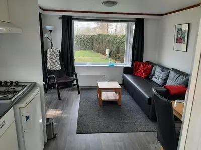 a living room with a black couch and a window at Chalet dichtbij zee en duinen in Heemskerk