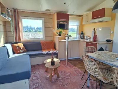 a living room with a blue couch and a kitchen at Chalet aan zee in Noordwijk aan Zee