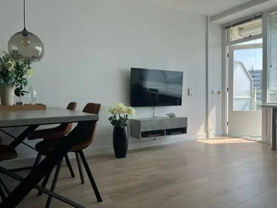 a living room with a table and a television on a wall at Blue Fish in Zandvoort