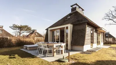 a small house with a thatched roof with a table and chairs at Dutchen Vakantiepark Duynvallei in Schoorl