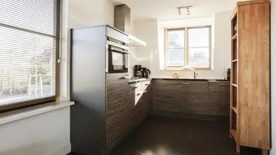 a kitchen with wooden cabinets and a large window at Dutchen Vakantiepark Duynvallei in Schoorl