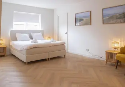 a white bedroom with a bed and two windows at Sint Adelbertus in Egmond-Binnen
