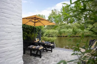 a patio with a table and an umbrella next to a pond at Loft 48 in Haastrecht