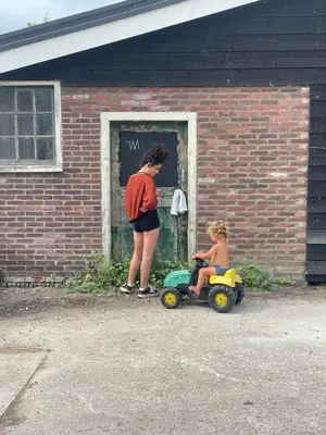 a woman standing next to a child in a toy car at Vintage caravan in old orchard at farm Huize Blokland in Hem