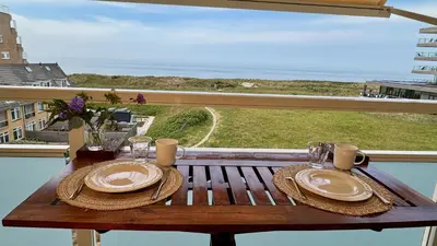 a table with plates and glasses on a balcony with the ocean at Strand Panorama Egmond in Egmond aan Zee