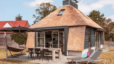 a thatch roofed house with a table and chairs at Dutchen Park Weideduyn in Schoorl