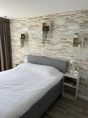 a bedroom with a white bed and a stone wall at Burgervlotbrug aan zee met sauna in Burgerbrug