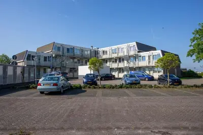 a parking lot with cars parked in front of buildings at Burgervlotbrug aan zee met sauna in Burgerbrug