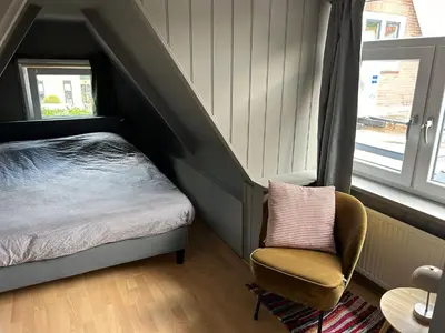 a bedroom with a bed and a chair and a window at Westerhuysje in Uitgeest