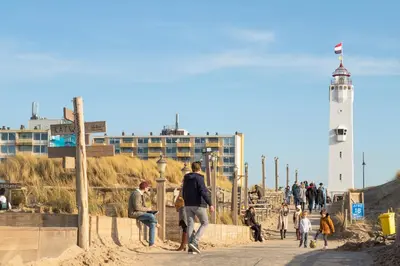 a group of people walking on the beach with a lighthouse at Guesthouse Porter Noordwijk in Noordwijk