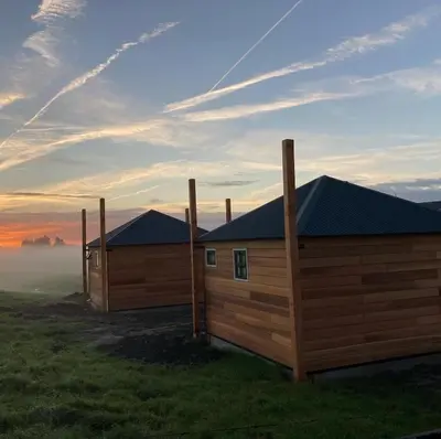 two wooden huts in a field with the sunrise in the background at Hooiberghut op boerderij in Leidschendam