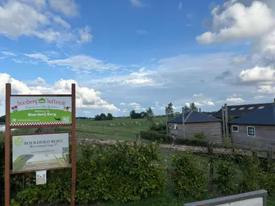 a sign in front of a farm with sheep in a field at Hooiberghut op boerderij in Leidschendam