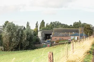 a farm with a field of grass and a fence at Hooiberghut op boerderij in Leidschendam
