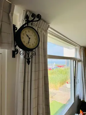 a clock hanging on a wall next to a window at Beachhouse Seepaertje - Boulevard Noordwijk aan Zee in Noordwijk aan Zee