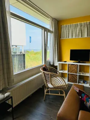 a living room with a chair and a tv and a window at Beachhouse Seepaertje - Boulevard Noordwijk aan Zee in Noordwijk aan Zee