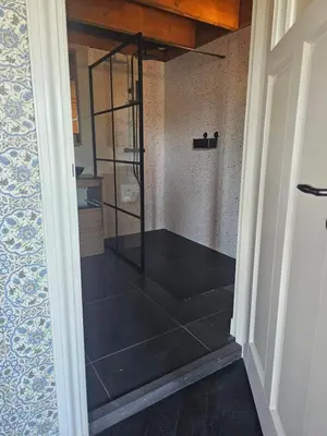 a glass shower in a room with a tile floor at De Gouwe Hooiberg in Hoogwoud