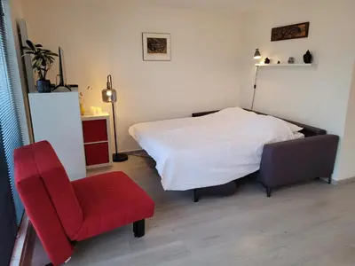 a bedroom with a bed and a red chair at Bright room with kitchen in Amsterdam