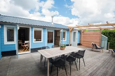 a blue house with a wooden deck with a table and chairs at Westeindercabin, rustige locatie maar naast Amsterdam & Schiphol in Aalsmeer