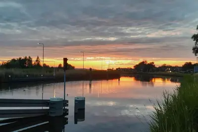 a body of water with a bench in front of a sunset at Onder de Kastanje! in Koedijk