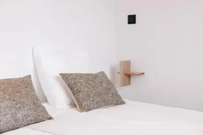 a white bed with two pillows and a cross on the wall at Bella Beach House in Zandvoort