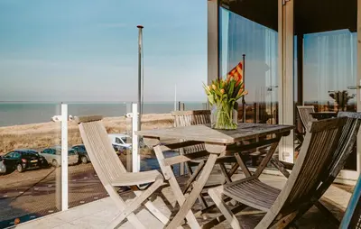 a wooden table and chairs on a balcony with the beach at Appartement Crab in Egmond aan Zee
