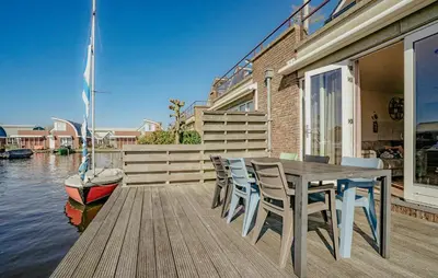 a wooden deck with a table and chairs and a boat at Westergeest 3 6P in Uitgeest