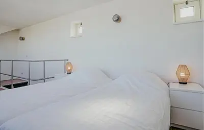 a white bedroom with a large white bed with two lamps at Kraaijennest in Uitgeest