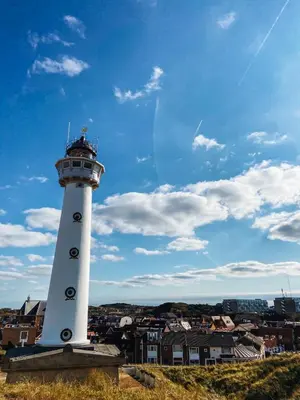 a lighthouse on a hill with a city in the background at Vakantiehuisje aan Zee - 100m van Strand in Egmond aan Zee