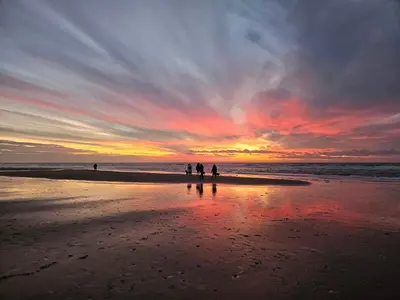 a group of people walking on the beach at sunset at Vakantiehuisje aan Zee - 100m van Strand in Egmond aan Zee