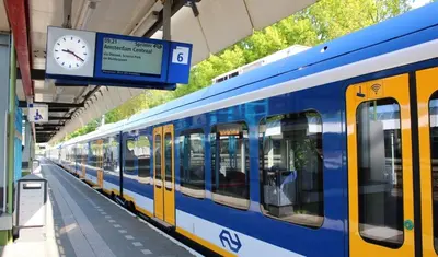a blue and yellow train at a train station with a clock at The Duck of Amsterdam in Amsterdam